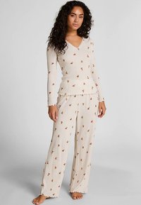 Lange mouwen, crèmekleurig pyjama-set met geribbelde structuur en bloemenpatroon. De top heeft een V-hals en de broek heeft een ontspannen pasvorm met gegolfde randen.