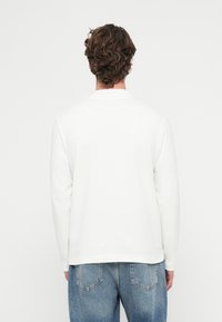 Biała koszula z długim rękawem i okrągłym dekoltem, wykonana z bawełny, zestawiona z jasnobłękitnymi dżinsami o luźnym kroju i tylnych kieszeniach.