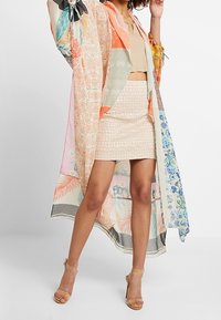 Mnohobarevný kimono s květinovými a geometrickými vzory, poloprůhledná látka, dlouhé rukávy a ozdobné mašle. V páru s strukturovanou béžovou sukní.