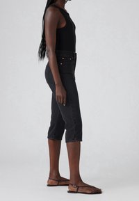 Top de tirantes negro con texturizado acanalado combinado con pantalones capri de mezclilla negros de cintura alta con dobladillo recortado y cierre de doble botón. Sandalias planas con tiras.