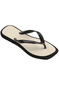 Une seule tong beige avec une semelle noire et des brides noires texturées inclinée pour montrer le nom de la marque sur la bride.