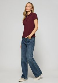 Burgundy pikétröja med kort ärm, med en diskret logotyp, i kombination med vida blå jeans och avslappnade beige sneakers.