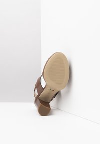 Brown heeled sandal with a textured sole, featuring dual straps. The shoe has a curved heel and a smooth beige sole. Designed for comfort.