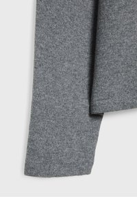 Gros plan sur un pull tricoté gris, présentant une texture lisse, des poignets côtelés et un design légèrement surdimensionné. Surface uni sans motifs.