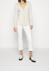 Lichtbeige geribde cardigan met een diepe V-hals en knopen aan de voorkant, gecombineerd met witte cropped broeken en bicolor instappers.