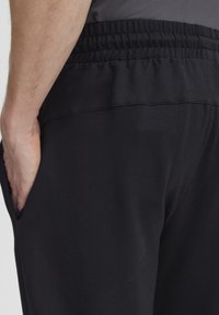 Zwarte sportbroek met een elastische tailleband, zijzakken en een gladde, elastische stof. Minimalistisch ontwerp zonder zichtbare patronen.