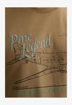 T-shirt in cotone marrone con ricamo azzurro chiaro della scritta "Pme Legend" e una grafica nera di un aereo con il testo "Exploring the Elements."