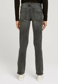 Mörkgrå denimjeans med slim fit, femfickorsdesign och subtila slitningar, tillsammans med vita sneakers.