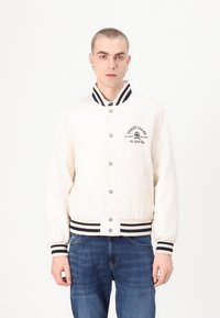 Kremfarget bomberjakke med svart stripete krage og mansjetter, med frontknapper og broderte logodetaljer.