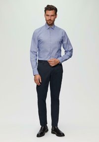 Lichtblauw overhemd met een smalle streepjespatroon, gedragen met donkerblauwe broek en zwarte leren schoenen, staand tegen een neutrale achtergrond.