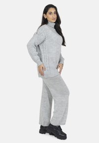 Maglione grigio chiaro realizzato a maglia con collo alto e dettagli a treccia, abbinato a pantaloni grigi a gamba larga, completato da stivali neri.