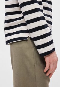 Ριγέ μακρυμάνικο πουκάμισο σε μπεζ και ναυτικό μπλε, με απαλή υφή. Συνδυασμένο με ελαιόχρωμο παντελόνι, εμφανίζει πλάγια άποψη και λεπτομέρεια με σχιστό στρίφωμα.