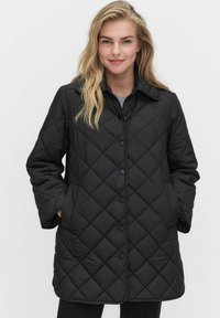 Svart vadderad jacka med skjortkrage, framknappar och långa ärmar. Tyget är slätt med en vadderad textur.