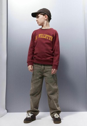 Bordo sporta krekls ar uzrakstu "LA VILLETTE", pelēkas militārā stila bikses, tumši sneakeri un antracīta krāsas cepure. Gluda tekstūra ar brīvu piegriezumu.