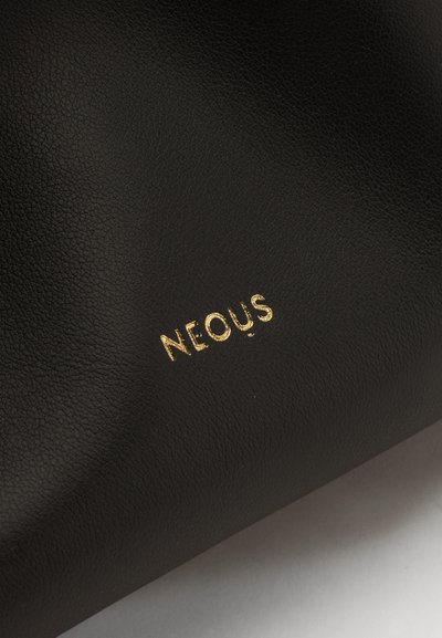 Gros plan de cuir noir texturé avec des lettres dorées en relief épelant "NEOUS" sur la surface.