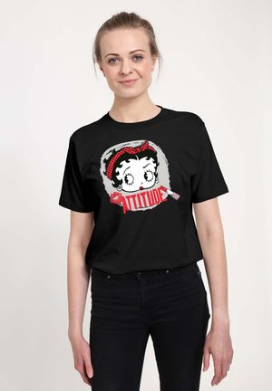 Sort T-shirt med en tegneseriefigur med et rødt prikket pandebånd og ordet "ATTITUDE" i fed rød skrift. Blødt stof.