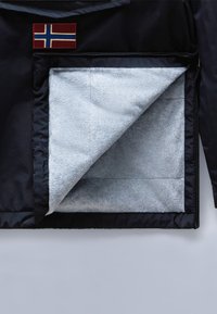 Giacca nera con un rivestimento in pile grigio testurizzato visibile. Presenta una toppa con bandiera rossa e blu nella zona del petto e una chiusura con zip.