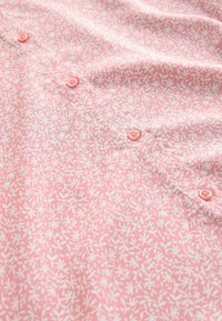 Rosa tyg med ett vitt blommönster, prytt med små knappar i matchande färg, slät textur och en något rynkad yta.