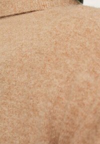 Beżowa dzianinowa tkanina swetra o gładkiej fakturze, z ribbanym kołnierzem i delikatnym, drobinkowym wzorem w całej konstrukcji.