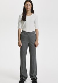 Top bianco a coste con maniche corte, abbinato a pantaloni grigi a vita alta. I pantaloni hanno una chiusura con bottone e una texture liscia. Scarpe nere.