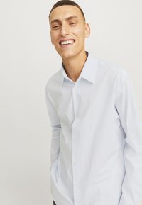 Ανοιχτό μπλε πουκάμισο με ρίγες, με μακριά μανίκια και κλασικό γιακά, διαθέτοντας λευκά κουμπιά και άνετη εφαρμογή.