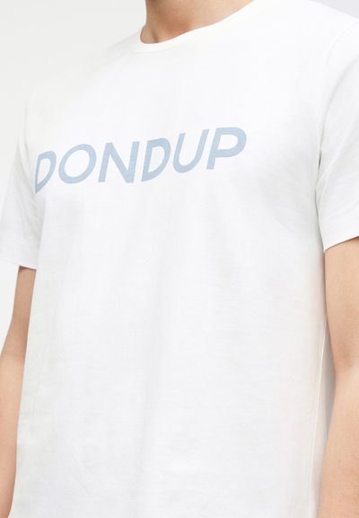 Άτομο που φοράει λευκό μπλουζάκι με στρογγυλή λαιμόκοψη και ανοιχτό μπλε κείμενο "DONDUP" στο στήθος, με το κάδρο να κόβει κάτω από το πηγούνι και μέχρι το μέσο του μπράτσου.