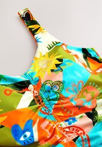 Rochie fără mâneci, colorată, cu un amestec de modele vii, inclusiv flori și forme geometrice, pe un fundal de țesătură netedă și mătăsoasă.