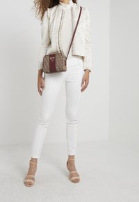 Quiltad vit jacka med volangkrage, ihopparad med vita byxor och ljusbruna remsandaler. Brun och beige mönstrad axelremsväska.