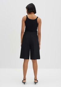 Schwarzes Tanktop mit dünnen Trägern, kombiniert mit hochgeschnittenen schwarzen Culottes. Glattes Material, weit geschnittene, knielange Shorts, akzentuiert mit einem Gürtel.