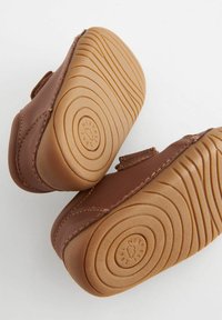 Chaussures pour tout-petits en cuir marron avec une semelle en caoutchouc souple tan, présentant un motif de bande de roulement ondulé et une fermeture à scratch.