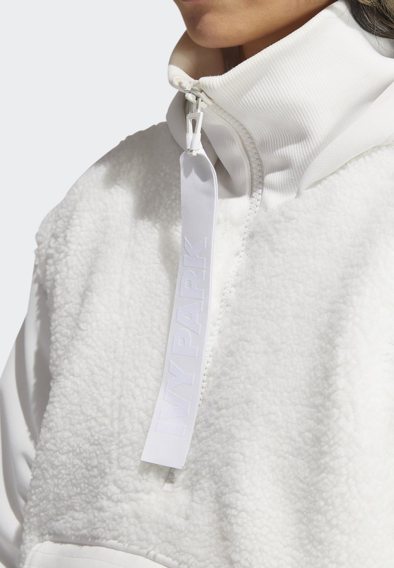 Biała polarowa bluza typu quarter-zip z prążkowanym kołnierzem, z naszywaną metką z logo i miękką teksturą na korpusie.