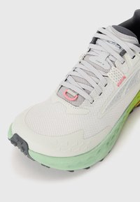 Light gray and green running shoe with mesh upper, white laces, pink accent, and branded label on the tongue reading "Timp 5".