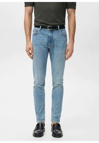 Vaaleansiniset farkut kapealla istuvuudella, viiden taskun mallilla ja hillityllä haalistuksella. Päällä musta nahkavyö ja mustat kengät.