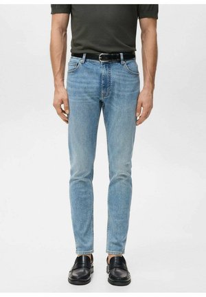 Vaqueros de mezclilla azul claro con corte ajustado, diseño de cinco bolsillos y un sutil desgaste. Llevados con un cinturón de cuero negro y zapatos negros.