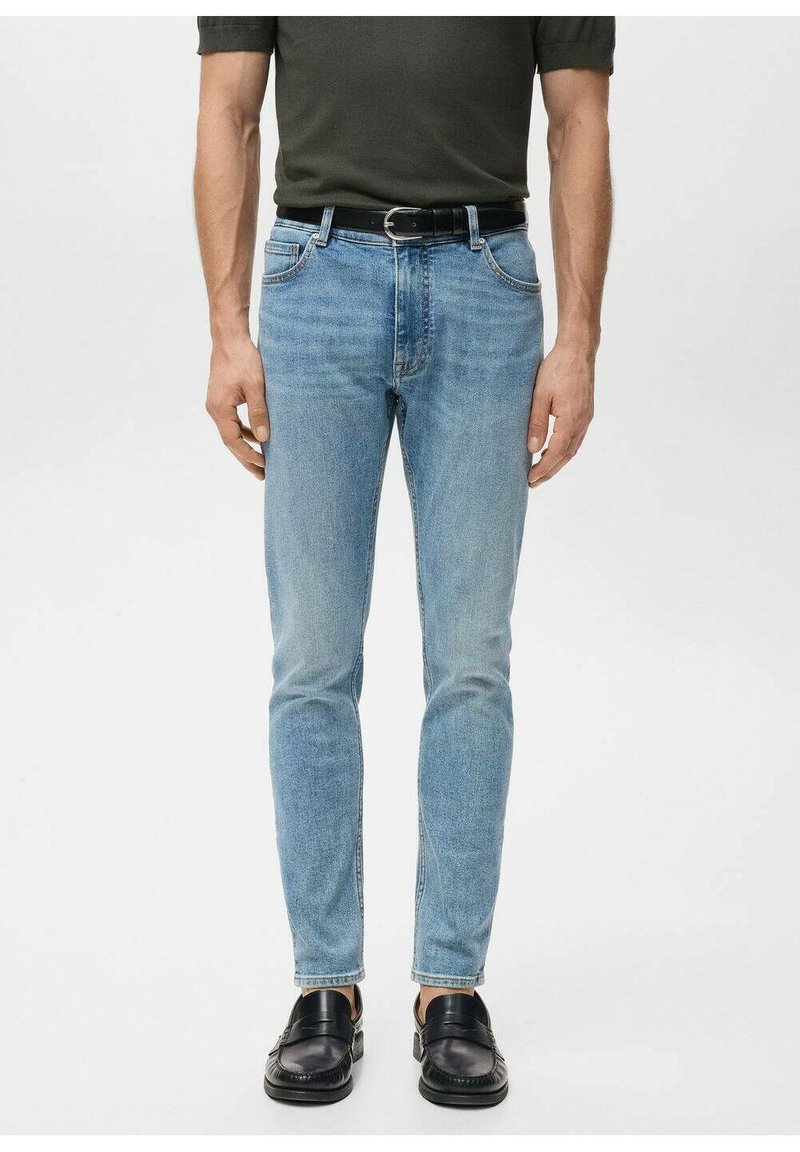 Vaaleansiniset farkut kapealla istuvuudella, viiden taskun mallilla ja hillityllä haalistuksella. Päällä musta nahkavyö ja mustat kengät.