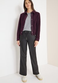 Bordeauxrode zachte jas met een kraag, grijs T-shirt eronder en zwarte faux leren broek. Sneakers met een gestructureerd detail.