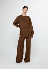 Brun stickad topp och vida byxor med en unik design, med dekorativa knappar längs sömmarna och en texturerad yta.