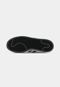 Black rubber shoe sole with zigzag tread pattern, featuring a grey side stripe and white accents. Smooth texture and rounded shape.