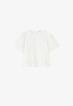 Blouse blanche à manches courtes avec bords festonnés et détails de découpe florale ajourée, col rond et manches légèrement bouffantes.
