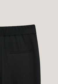 Zwarte broek met een elastische tailleband, voorzien van een vlakke voorkant en een horizontale achterzak. Gladde stof met een matte afwerking.