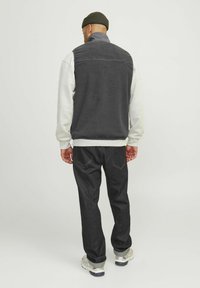Grijze fleece vest met een hoge kraag over een crèmekleurig longsleeve shirt, gedragen met donker denim jeans en lichte sneakers. Getextureerd en casual ontwerp.