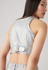 Cropped metallic denim top in light blue with a smooth texture. Features a rectangular buckle accent at the back and sleeveless design.
