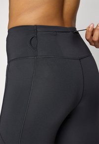 Leggings neri a vita alta con una texture liscia, dotati di una tasca sul retro e di un cordino per una vestibilità regolabile.