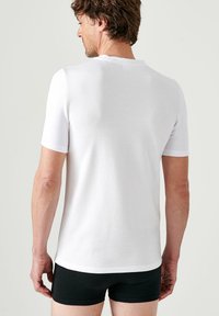 Witte t-shirt met korte mouwen van gladde katoen, met een klassieke pasvorm en een ronde halslijn, gedragen met zwarte shorts.