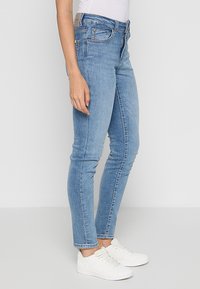 Jean skinny bleu clair en denim, avec fermeture éclair et bouton, poches avant, et finition délavée. Portés avec des baskets blanches.
