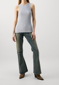 Top in cotone grigio a coste con scollatura rotonda, abbinato a jeans svasati blu sbiaditi e stivali alla caviglia marroni con tacco. Elementi di design minimalista.
