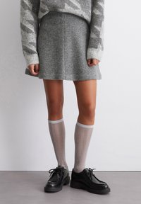 Grijze wollen rok met een zachte textuur, gecombineerd met glanzende, geribbelde kniehoge sokken en zwarte veterschoenen. Schone, minimalistische stijl.