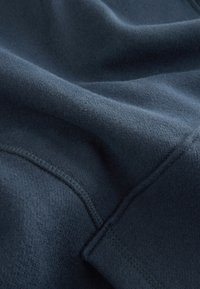 Marineblauer Fleece-Stoff mit weicher Textur, sichtbaren Nähten und einer leicht unebenen Oberfläche, die W�ärme und Komfort vermittelt.
