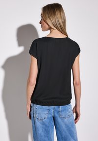 Svart kortärmad topp med lös passform och elastisk midja, parat med ljusblå denimjeans med bakfickor.