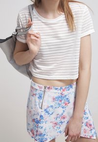 Chemise courte rayée blanche associée à une mini-jupe à motifs floraux avec des fleurs bleues et roses et un détail de fermeture éclair latérale.